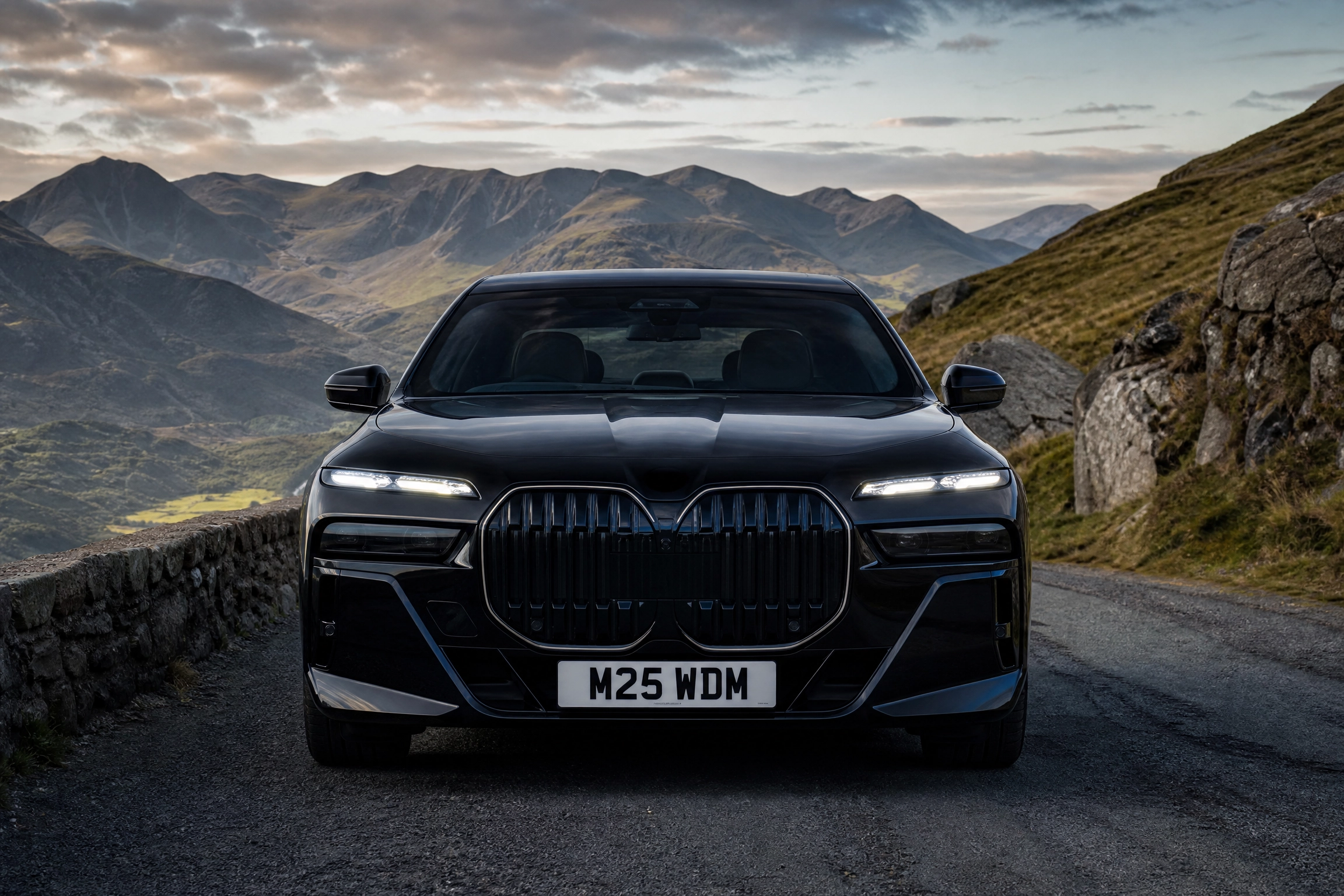 Chauffeur Service in Thorne by M25 Chauffeurs Ltd M25 Chauffeurs Ltd Professional Chauffeur Service United Kingdom Front view of a black SUV with a glossy grille parked on a mountain road, rocky slopes behind it and a stone barrier to the left, license plate M25 WDM visible.